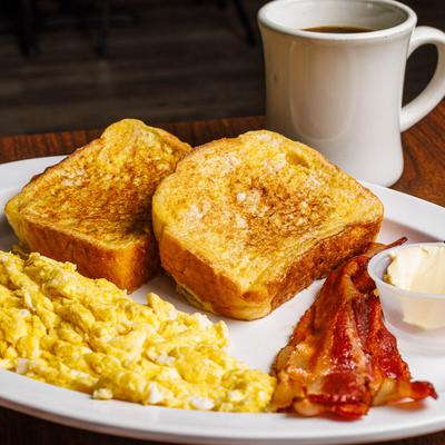 Breakfast plate with scrambled eggs, bacon, French toast, butter, and coffee.