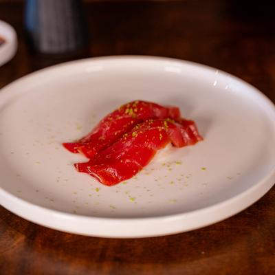 Soy-marinated tuna nigiri pieces on a white plate.