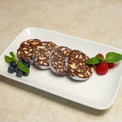 Chocolate salami slices arranged on a white plate with berries and mint garnish.