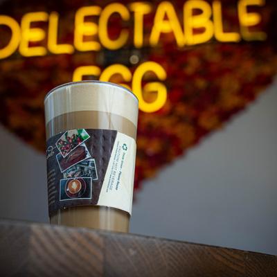 A glass of Latte with Delectable Egg neon text in the background.