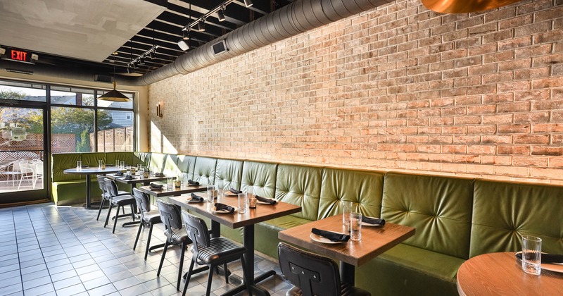 Interior, long corner banquette bench, tables and chairs ready for guests, red brick wall