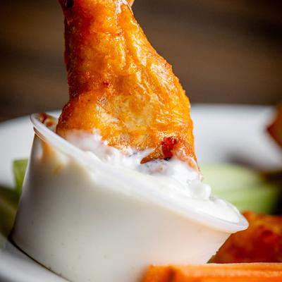 A chicken wing being dipped into blue cheese dip.