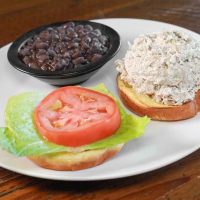 Chicken salad sandwich with lettuce and tomato, served with a bowl of black beans.