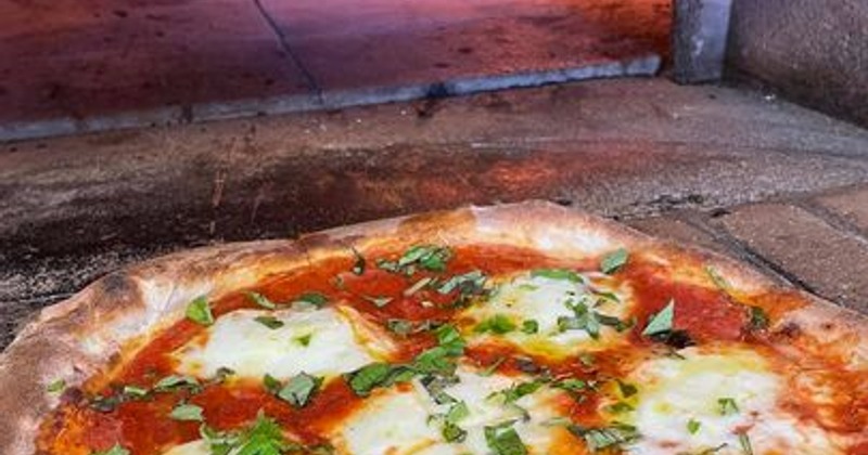 Margherita pizza inside a pizza oven with visible flames in the background