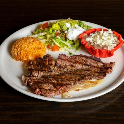 Grilled steak with salad, sour cream, guacamole, rice, and beans.
