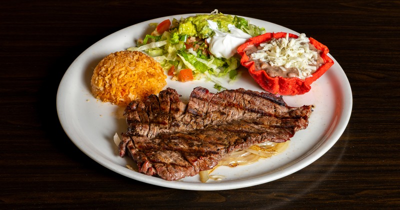 Grilled steak with salad, sour cream, guacamole, rice, and beans