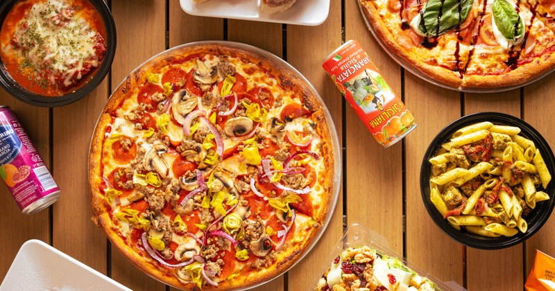 A spread of dishes, including two pizzas, pasta, salads, sandwiches, and cannoli