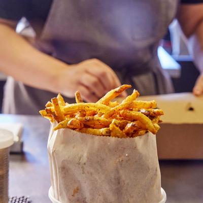 A serving of french fries, with an employee in the background preparing a takeout box.