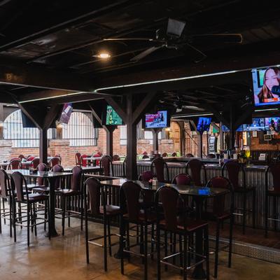 Spacious bar with high tables and red chairs, multiple TVs displaying various programs.