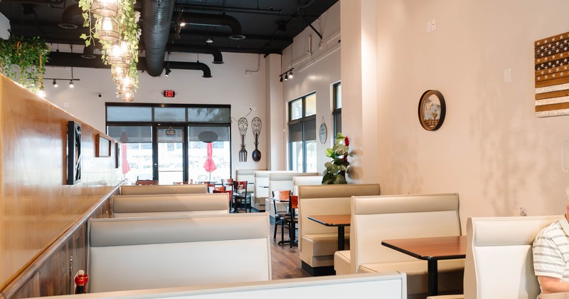 Interior of a modern restaurant with beige booths, hanging lights, and decorative wall pieces.
