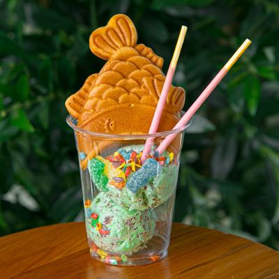 Ice cream with candy and a fish-shaped waffle cone in a clear cup.