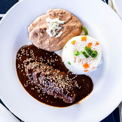 Poached chicken breast topped with a dark mole, served with rice and beans.