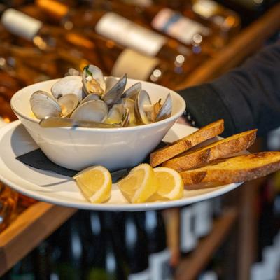Bowl of steamed clams with lemon wedges and toast on a plate.