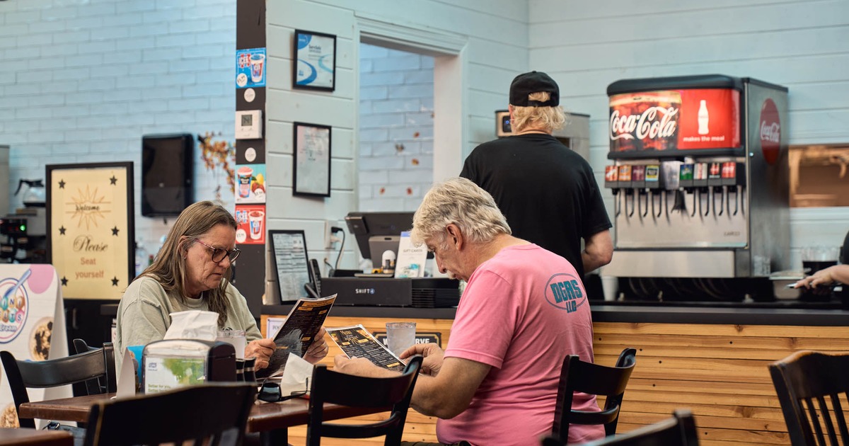 Two people at a table while another person stands by the counter