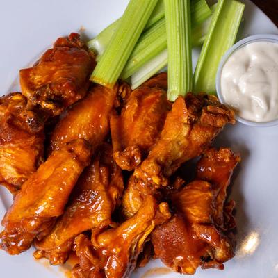 A top view of a plate with wings , celery and sauce.