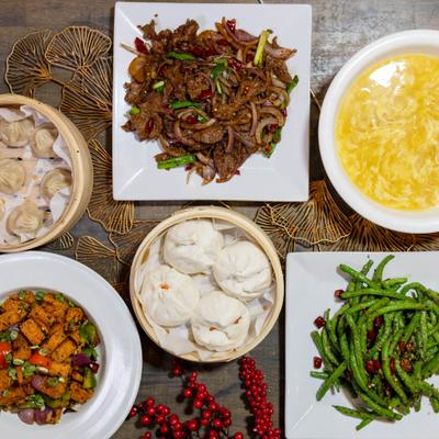 Chinese food spread with dumplings, steamed buns, beef stir-fry, and green beans.