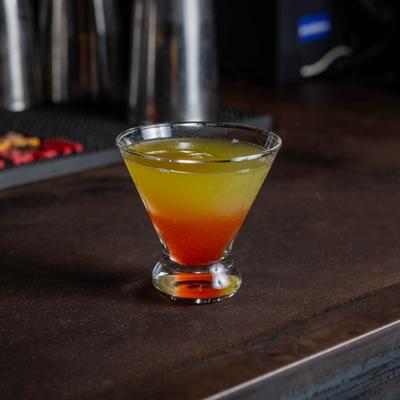A yellow and orange vodka cocktail served in a cosmopolitan glass on a bar counter.