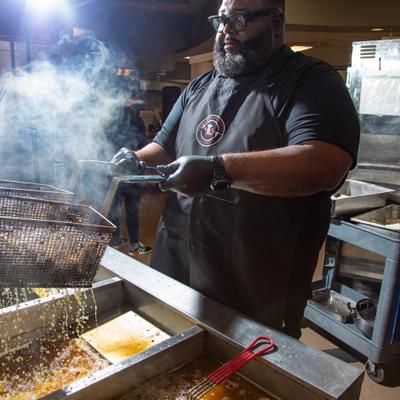 Cook lifting a fryer basket from hot oil.