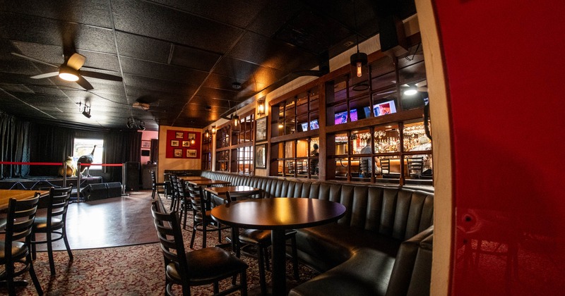 Interior view of a bar with a stage, tables with chairs, and a cushioned bench