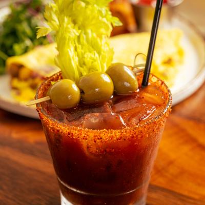 Glass of Bloody Mary, garnished with olives and celery.