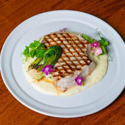 Grilled swordfish filet over potato puree on a white plate , Bok choy and flower garnish.