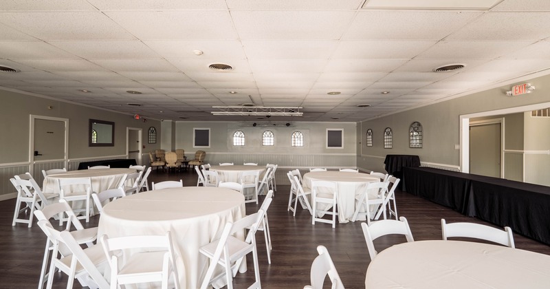 Empty event hall with round tables, white chairs, beige chairs in the back