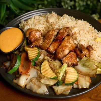 Hibachi chicken with stir-fried vegetables, fried rice, and a cup of orange sauce.