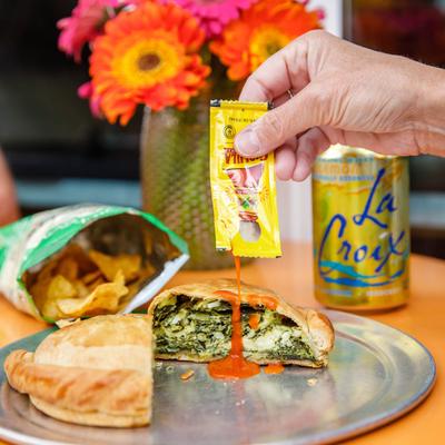 Spinach pasty, with sauce and a bag of potato chips.