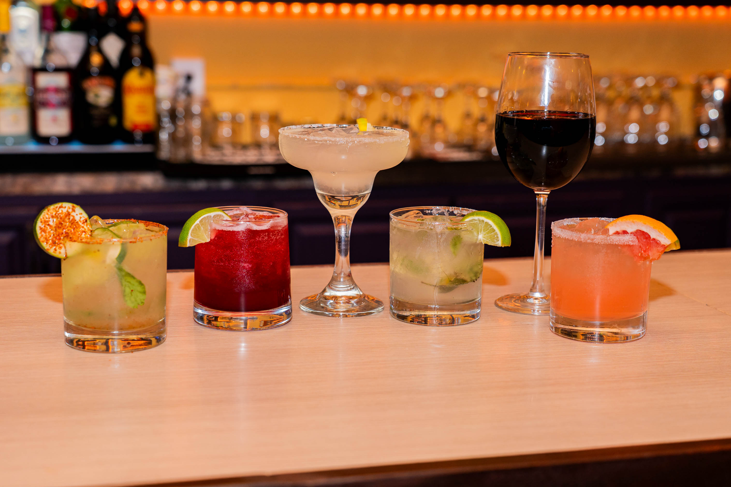 Various cocktails served on a bar counter with a glass of red wine