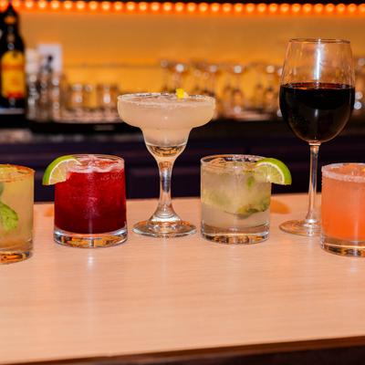 Various cocktails served on a bar counter with a glass of red wine.