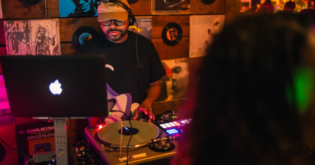 DJ playing music in front of a wooden wall with vintage record covers and records