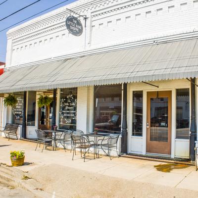 Storefront featuring a covered metal awning and outdoor sidewalk bistro seating.