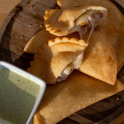 Empanadas on a wooden board with a dish of green sauce.