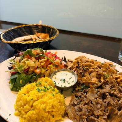 Shredded meat with yellow rice, salad, and yogurt sauce on a table.