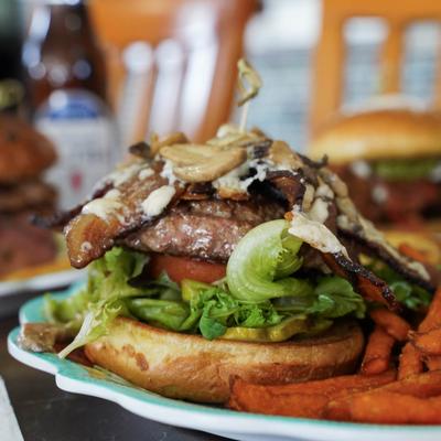A towering burger with lettuce, tomato, pickle, mushrooms, bacon, and cheese.