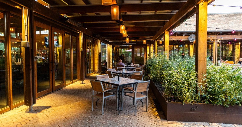 Outdoor, patio, wooden pergola, hanging lights, tables, chairs, planter box with greenery