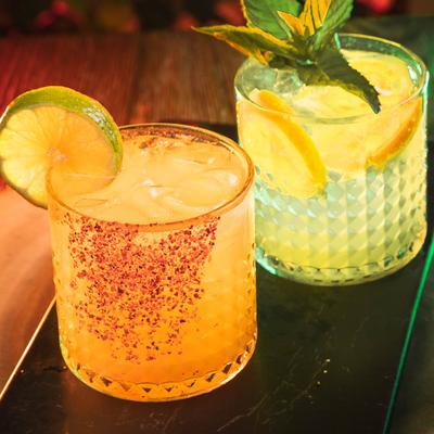 Two colorful cocktails in textured glasses on a table.