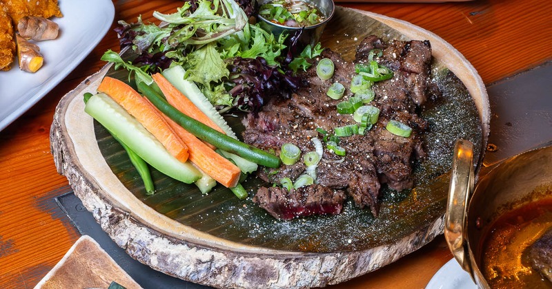 Assorted food dishes on a table with flat steak salad as the centerpiece