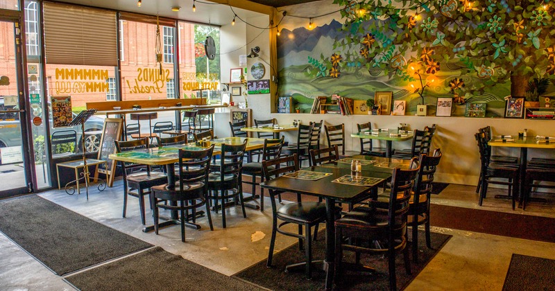 Interior of a cozy restaurant with large windows, wooden tables, and a colorful mural on the wall