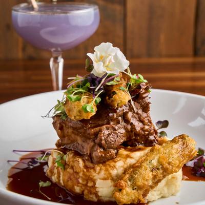 Braised beef short ribs with garlic mashed potatoes, alongside a cocktail.