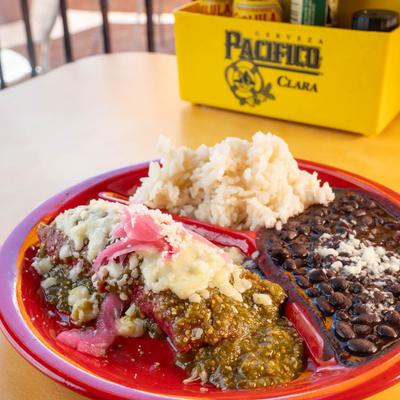 Plate of a chicken enchilada served with rice and black beans on the side.