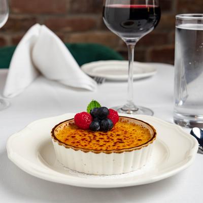 Creme Brulee garnished with berries and mint, served with a glass of red wine.