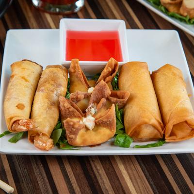 Crispy fried spring rolls and wontons with red dipping sauce on a white plate.