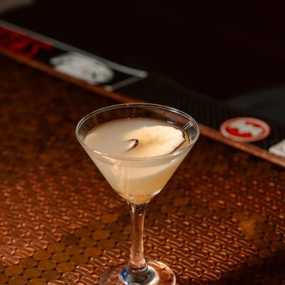 Light cocktail in a martini glass rests on a bar counter.