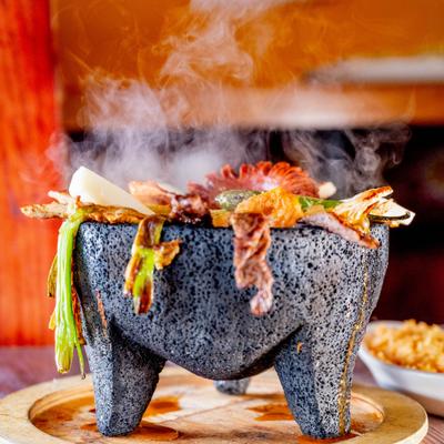 Steaming molcajete on a wooden platter, side view.