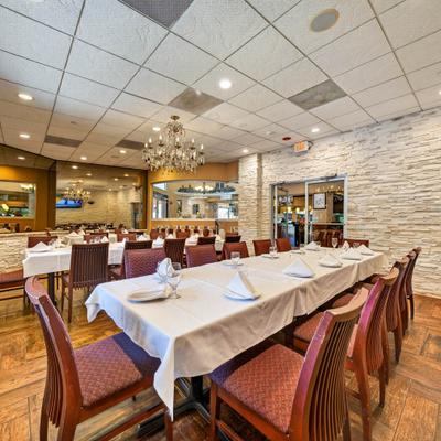 Interior with long tables arranged with white tablecloths and dark wooden chairs.