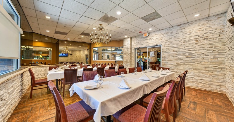 Dining area with white tablecloths, wooden chairs, chandelier, and faux stone walls