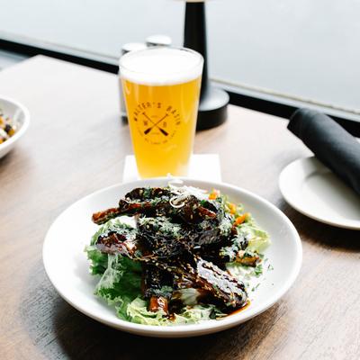 A plate of Sticky Ribs with a glass of  beer on a table.