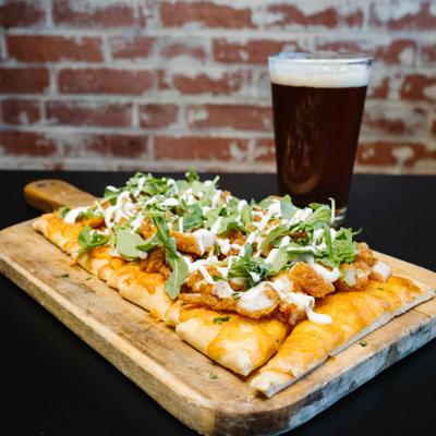 Flatbread with crispy chicken, arugula, and cheese, served with a beer.