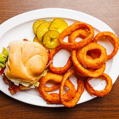 Bacon cheeseburger with lettuce served with onion rings and pickles.